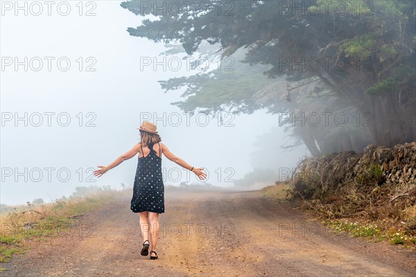 Tourist woman walking through the foggy path towards the juniper forest in El Hierro. Canary Islands