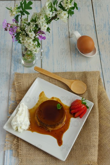 Egg custard with cream and strawberries on a white plate on a blue wooden table with flowers