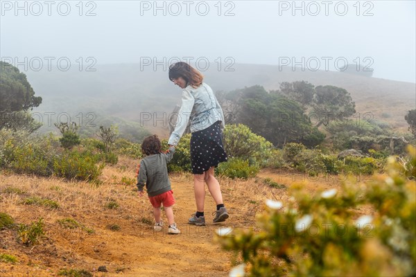 Mother and son walking with flowers to a Sabinar tree twisted by the wind of El Hierro. Canary Islands