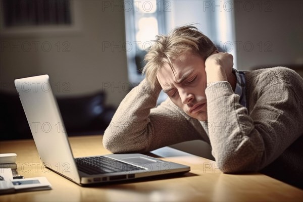 A man sits exhausted at a notebook