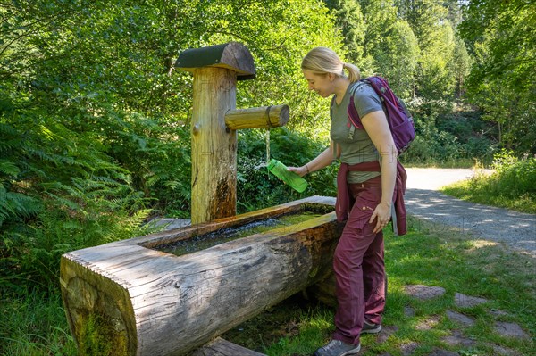 Hiking woman fills drinking bottle at the wooden fountain on the hiking trail Sprollenhaeuser Hut