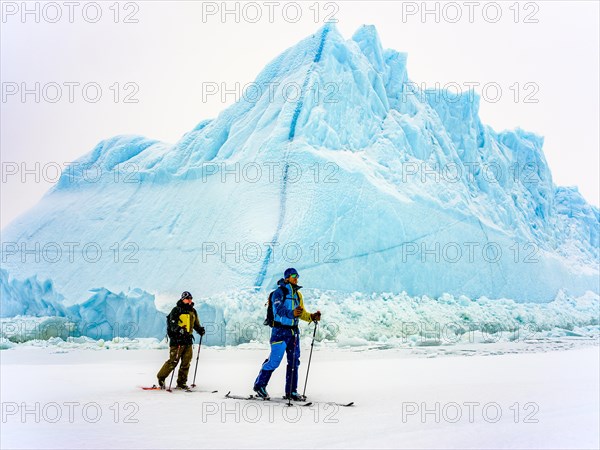 Ski tourers in front of iceberg in frozen Kong Oscar Fjord