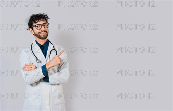 Smiling doctor pointing finger isolated. Doctor pointing at an isolated white space. Young doctor pointing finger at a blank space