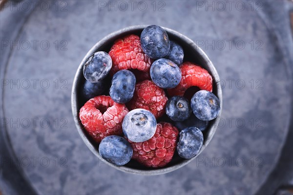 Top view of mixed blueberry and raspberry fruits in iron cup