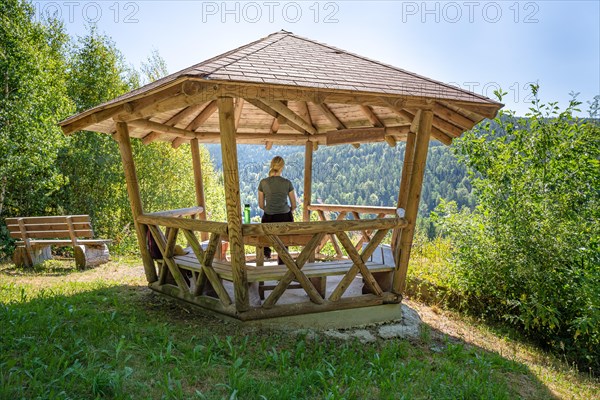 Woman eating pretzel in wooden pavilion and looking at the endless forest on the hiking trail Sprollenhaeuser Hut