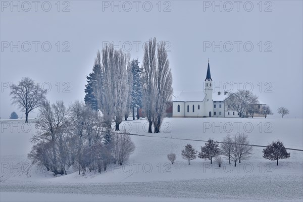 Small hamlet with chapel in snowy landscape in gloomy winter weather