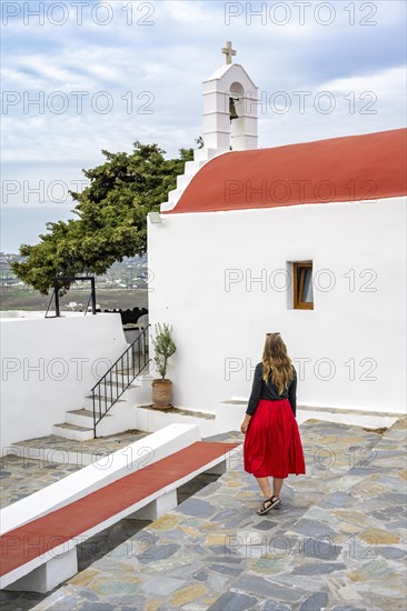 Young woman with red skirt at a Cycladic white and red Orthodox church
