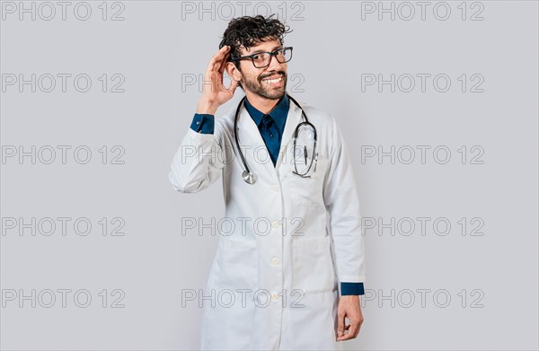 Smiling doctor listening to a rumor. Young doctor smiling with hand over ear isolated