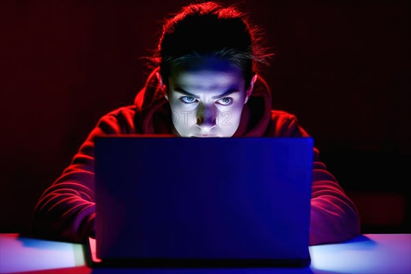 A young woman in her mid-20s works at her laptop at night