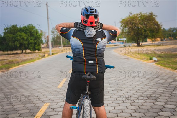 Rear view of a cyclist with neck pain with the bike. Back view of a cyclist man having neck pain while riding a bike