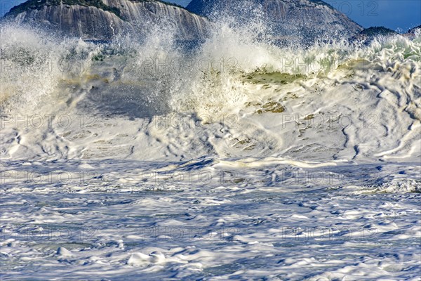 Beautiful and strong sea wave on the beach with water drops and foam splashing in the air on a sunny day