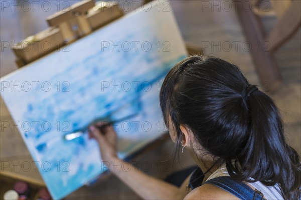 Woman artist painting on a canvas a blue abstract painting. Creative ywoman working on the floor in her art studio