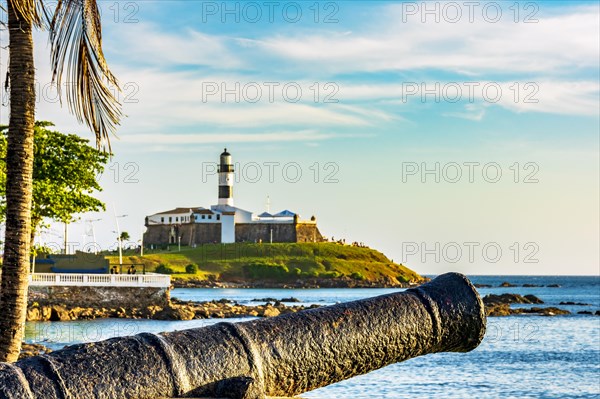 Old cannon and the Barra Lighthouse one of the main historical buildings and tourist spot in the city of Salvador in Bahia surrounded by the sea during the late afternoon.