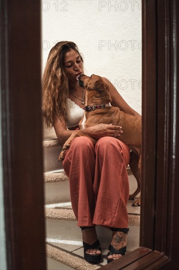 Beautiful young latina hugging her dog showing her affection on the stairs of her house. Love for animals