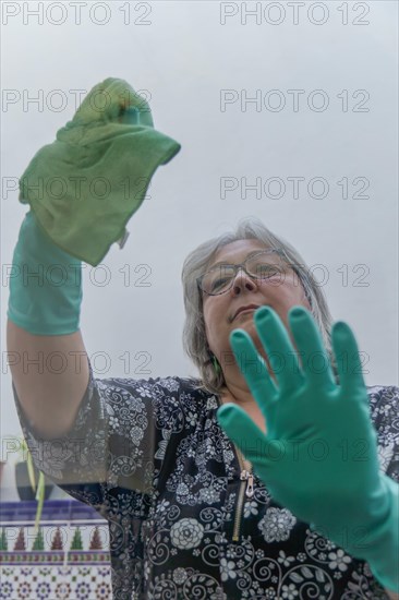 Closeup of a woman cleaning the windows of her house with a green rag and rubber gloves