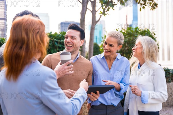 Cheerful group of coworkers laughing and looking at a tablet outdoors in a corporate office area