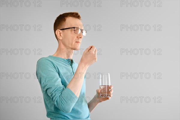 Middle aged man standing with a glass of water and takes pill from headache