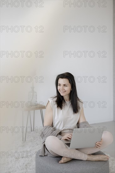 Young woman sitting comfortably with laptop on a stool in the living room