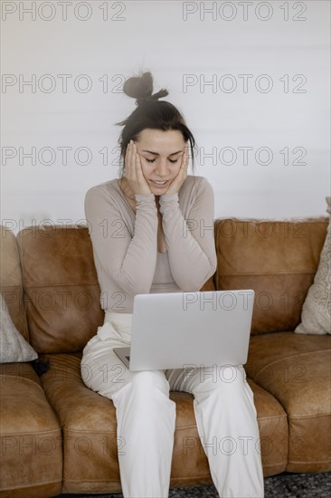 Woman sits on couch with laptop completely overwhelmed