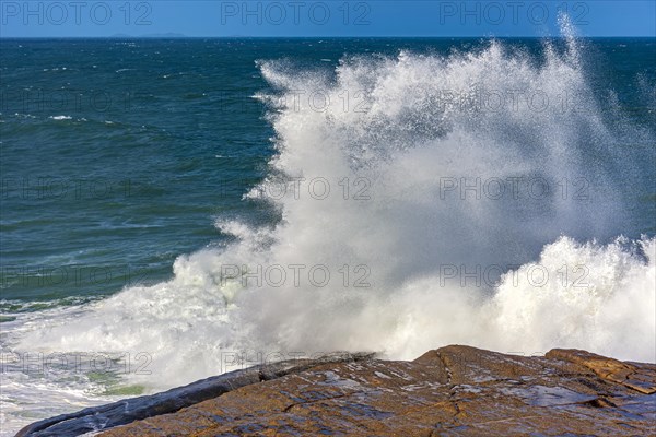 Wave breaking over rocks with water splashing with blue sky on a rough sea day in Rio de Janeiro
