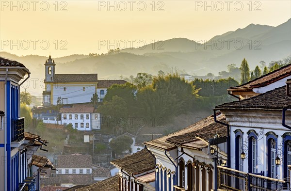 Facades of houses and church in colonial architecture in an old street in the city of Ouro Preto with the mountains in the background