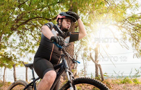 Exhausted chubby cyclist on his bike looking into the distance. Tired cyclist while riding the bike on a road