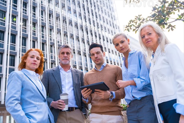 Portrait of cheerful group of coworkers laughing and looking at a tablet outdoors in a corporate office area