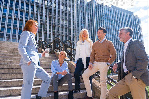 Cheerful group of coworkers outdoors in a corporate office area having a break time on the stairs