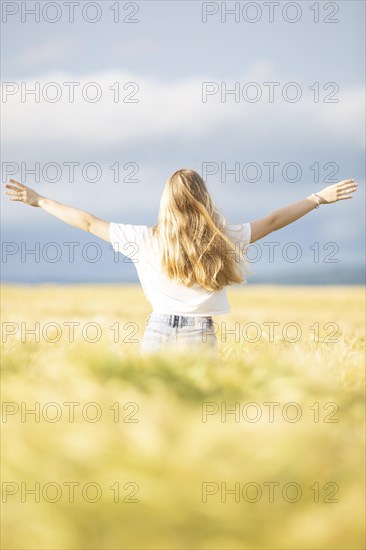 A young girl walks through a cornfield on a sunny warm day and spreads out her arms