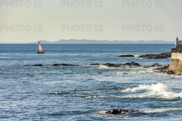 Rudimentary fishing boat sailing on the horizon during sunset in All Saints Bay in the city of Salvador