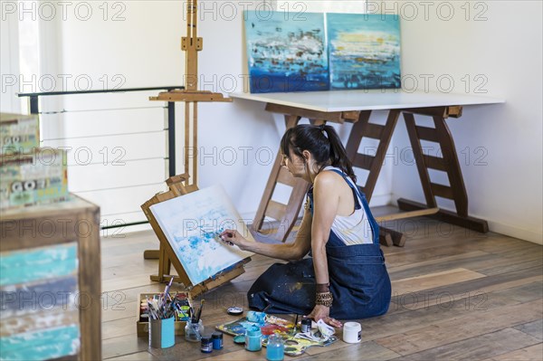 Woman artist painting on a canvas a blue abstract painting. Creative ywoman working on the floor in her art studio