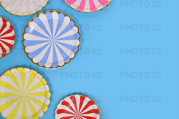 Colorful striped paper party plates on side of blue background with copy space