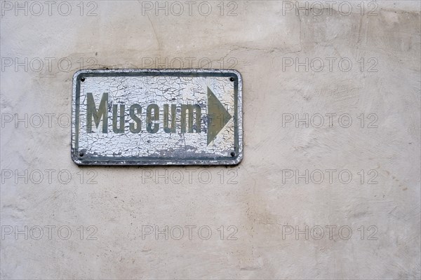 Yellowed and weathered sign full of chipped paint on which a signpost is painted with the inscription MUSEUM