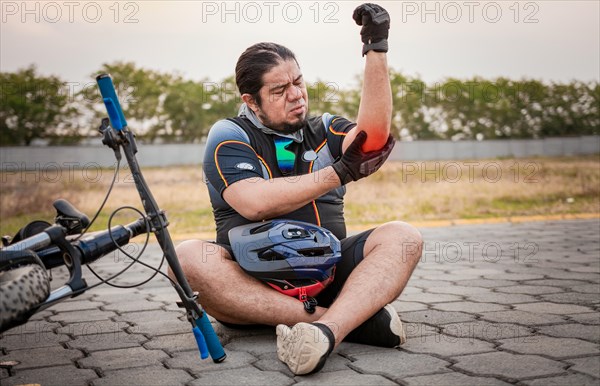 Accidented cyclist with elbow pain. Accidented cyclist man on the pavement in pain rubbing his elbow