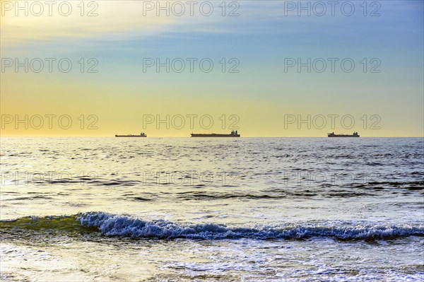 Ships moored on the horizon waiting to go to port during dawn on Ipanema beach in Rio de Janeiro