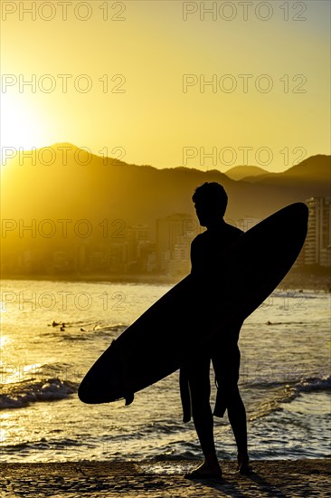 Surfer silhouette with his longboard looking at the Iapnema beach waves in Rio de Janeiro during sunset