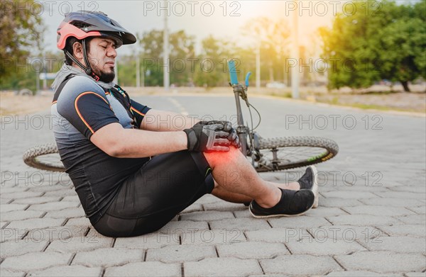 Cyclist with knee pain outdoors. Male cyclist sitting on the pavement with knee pain. Concept of a cyclist with knee injury outdoors