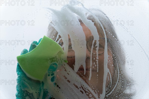 Closeup a woman cleans the glass with a green sponge and gloves