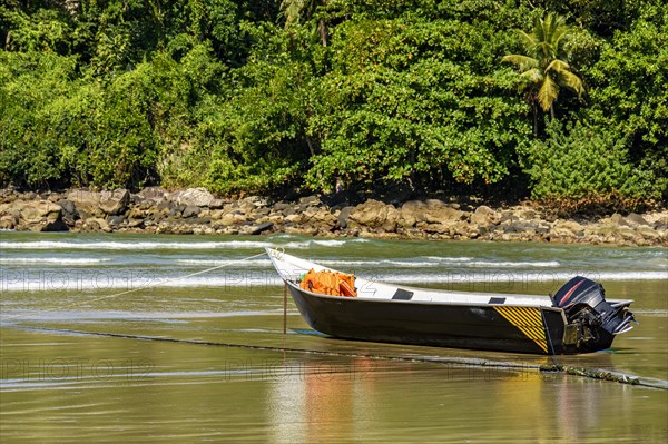 Speedboat standing on the sand of the beach with the rocks and rainforest in the background on a sunny day in Bertioga on the coast of the state of Sao Paulo