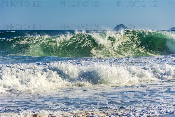 Sea wave crashing on the beach on a sunny day in summer with water drops and foam splashing in the air