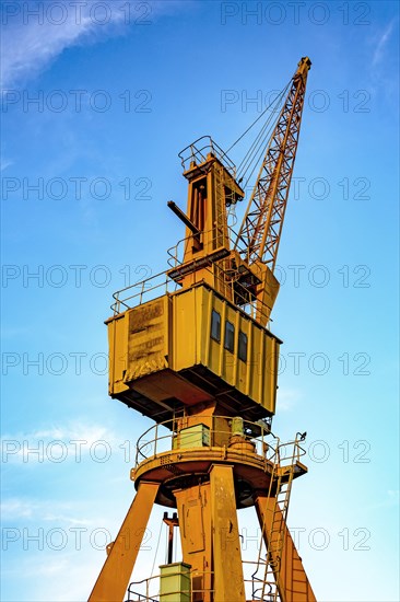 Old and obsolete yellow crane on the harbor pier with blue sky in the background.