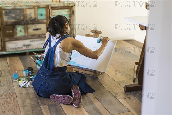 Woman artist painting on a canvas a blue abstract painting. Creative ywoman working on the floor in her art studio