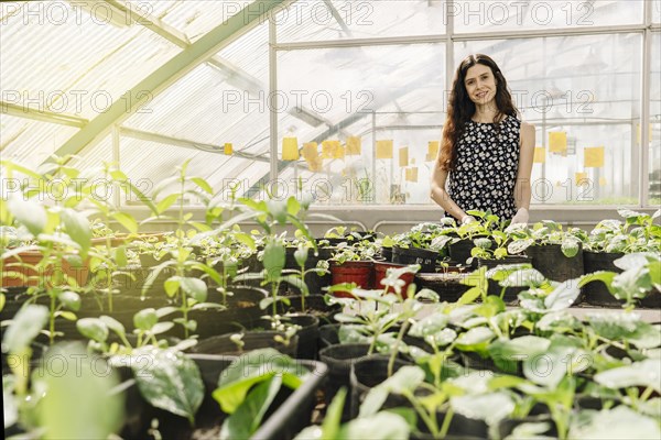 Female scientist examining plants in a greenhouse standing smiling and looking at camera. Large General View