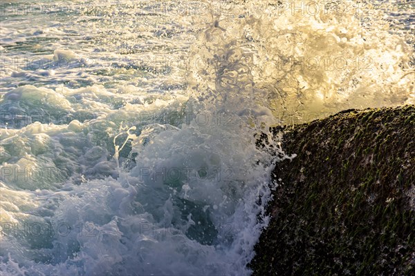 Water and sea foam splashing with waves crash against rocks during tropical sunset