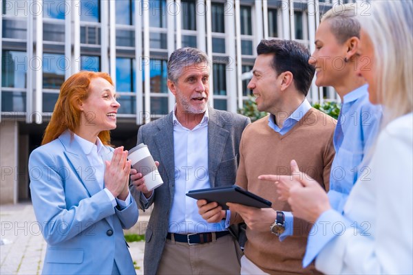 Cheerful group of coworkers laughing and looking at a tablet outdoors in a corporate office area