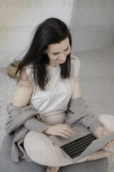 Young woman sitting comfortably with laptop on a stool in the living room