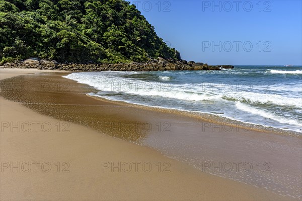 Paradisiacal rocky beach with clean and calm waters surrounded by forest and hills in Bertioga coast of Sao Paulo state