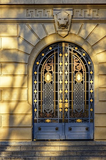 Old and imposing metal gate decorated with golden details with shadows and reflections of the late afternoon sun