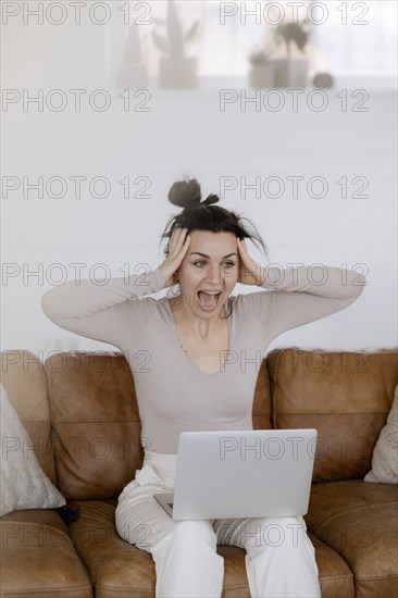 Woman sits on couch with laptop completely overwhelmed