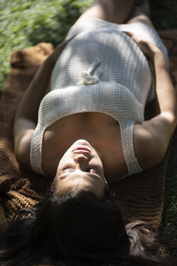 Pregnant Latina woman lying on the grass in a park